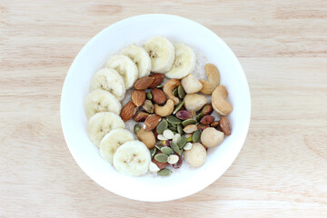 Overnight oatmeal with mixed nut and banana in the white bowl on the table