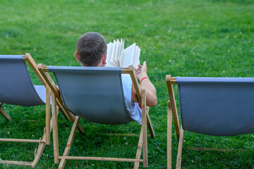 Mężczyzna leży na leżaku w ogrodzie i czyta książkę 