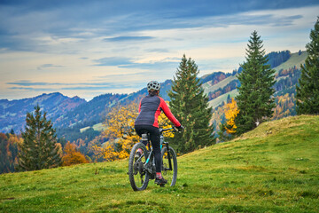 Fototapeta na wymiar pretty senior woman riding her electric mountain bike in autumn and enjoying the spectacular view over the Allgau and Bregenz Forest alps near Steibis, Bavaria, Germany