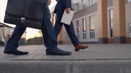 Business people walk along sidewalk, peoples walking feet. Office pedestrians walk along city street to work. City life of people. Man with briefcase in business suit walks next to business woman - obrazy, fototapety, plakaty