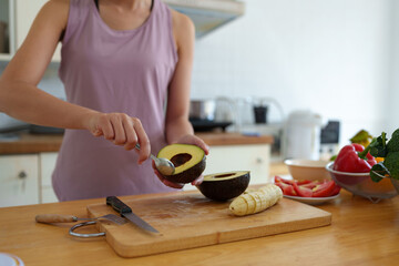 Confident young woman in exercise clothes preparing fruit Avocados for eating and live streaming on a laptop computer Introducing the benefits that affect body proportions Dieting for good health.