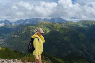 Fototapeta na wymiar A young girl in a yellow hoodie and cap, a traveler in the Polish Tatras, the sky in the clouds.