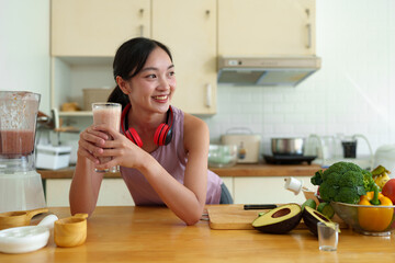 Young woman in Asian exercise clothes making a fruit and vegetable smoothie after a healthy workout at home. Concept of diet and healthy food, lifestyle