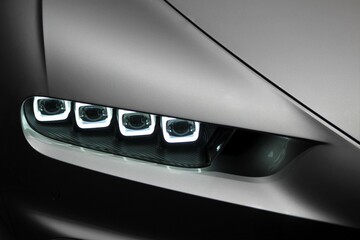Frontal closeup of modern gray car while the led lamps are on in low light that shows the style and design of the luxury car 