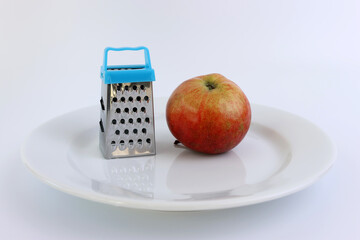 Hand held miniature grater and apple on a white plate.