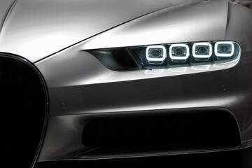 Frontal closeup of modern gray car while the led lamps are on in low light that shows the style and...