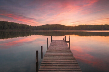Fototapeta na wymiar Beautiful empty wooden bridge over a lake with mountains, trees and a blue sky, generative ai 