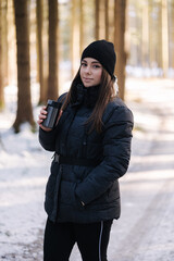 Beautiful woman thinking hot coffee from thermos in snowy forest 