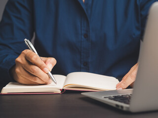 Businessman hand holding a pen and writing in a notebook while sitting in the office