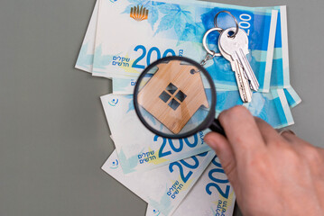 Buying a house, building repair and mortgage concept in Israel. Estimation real estate property with loan money and banking. Keys and house with shekel cash banknotes under magnifying glass. - obrazy, fototapety, plakaty