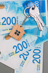Buying a house, building repair and mortgage concept in Israel. Estimation real estate property with loan money and banking. Keys and house with shekel cash banknotes.