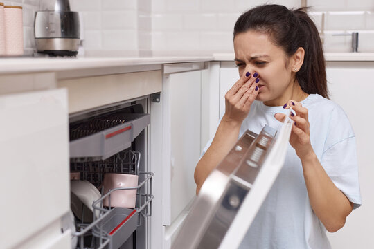 woman smells strange and terrible smell coming from dishwasher machine in kitchen