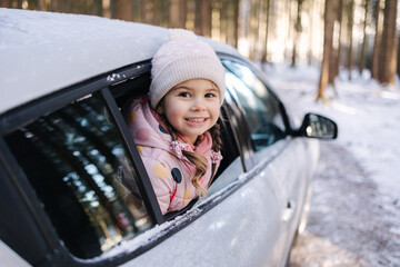 Adorable little girl looks out of the car window and looks at the beautiful snowy forest