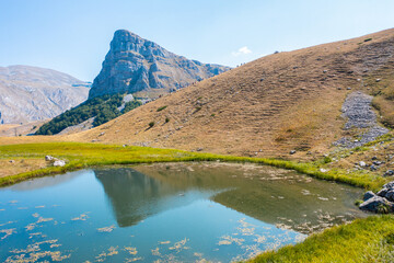 A lake with grass around it and a mountain peak reflected in the water