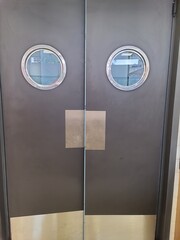 Entrance to the restaurant kitchen. Closed wooden double door with round porthole style window.
