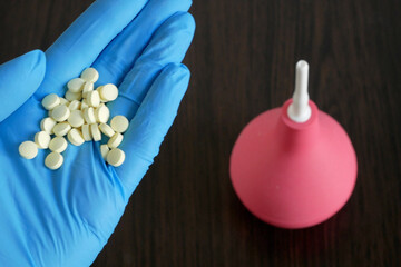 hand holding  pills on enema  on wooden background, enema vs pills for treatment  from intestinal...