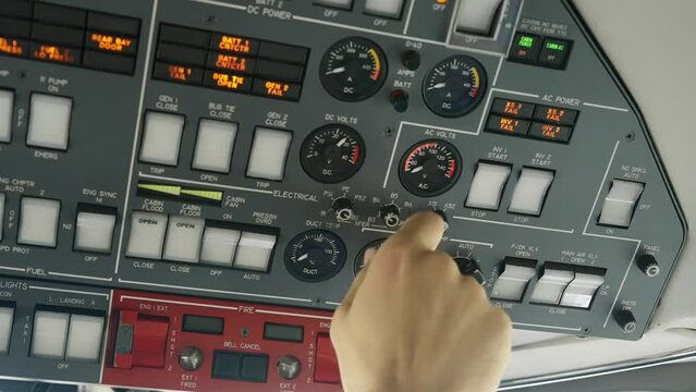 Cropped shot of pilot's hand turning knobs on overhead panel in private jet cockpit. Professional aviator checking DC voltage before flight