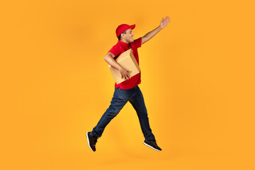 Fototapeta na wymiar Arab deliveryman leaping with cardboard box over yellow studio background