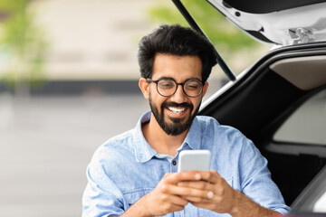 Closeup indian guy using smartphone, standing by car