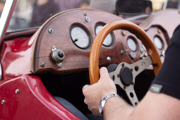 Man driving classic vintage old retro red car. Male hand on wooden brown steering wheel. Instrument...
