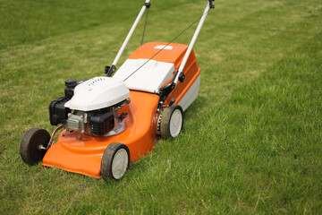 Top view of modern orange-grey electric lawn mower cutting bright lush green grass. Gardening work...