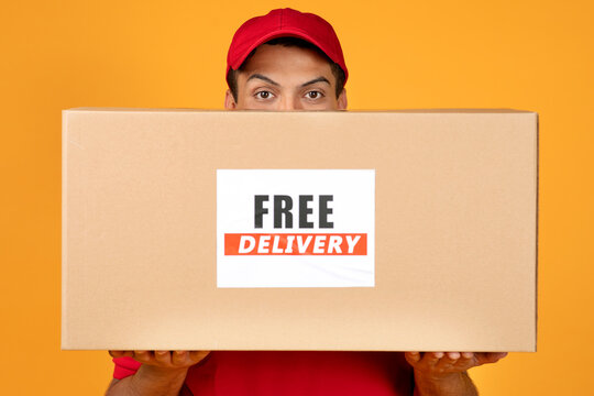 deliveryman peeking from cardboard box with Free Delivery label, studio
