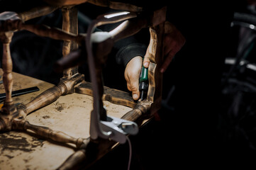 Male professional woodworker carpenter glues a chair, repairs furniture in the workshop. Photography, work concept.