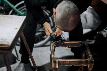 An adult male professional woodworker carpenter glues a chair, repairs, restores furniture in the workshop, clamping wooden products with a clamp. Photography, work concept, portrait.