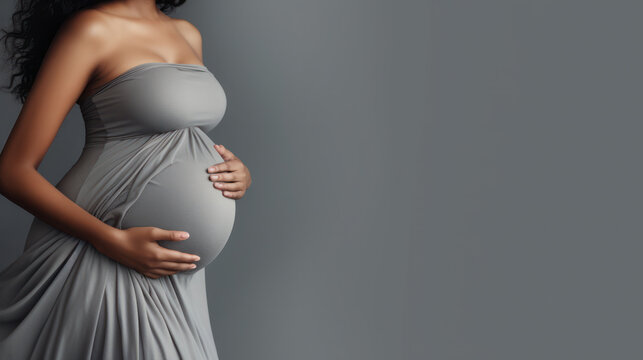 Pregnant African American Woman In Dress Holds Hands On Belly On A White Background. Pregnancy, Maternity, Preparation And Expectation Concept. Close-up, Copy Space, Indoors. Beautiful Tender Mood