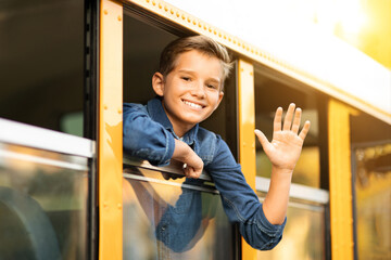 Happy preteen boy looking out of school bus window and waving hand - obrazy, fototapety, plakaty