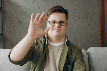 Young man with down syndrome in casual clothes record get video call talk use pc laptop sits on...