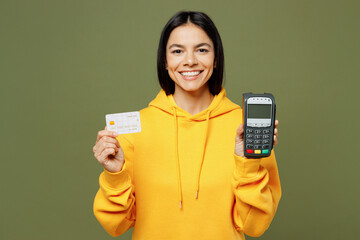 Young Latin woman wears yellow hoody casual clothes hold wireless modern bank payment terminal process acquire credit card isolated on plain pastel green background studio portrait. Lifestyle concept.