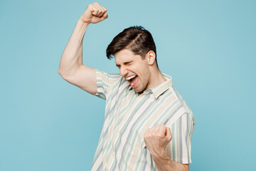 Young excited happy man wear striped shirt casual clothes doing winner gesture celebrate clenching...