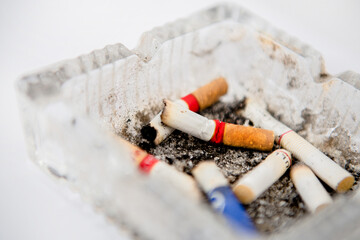 Close-up of cigarette butt in ashtray. Glass cigarette ashtray on white background. Concept of health and dangers of smoking.