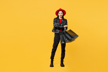 Full body stylish young woman wear casual clothes red hat hold shopping paper package bags hold hands crossed folded look camera isolated on plain yellow background. Black Friday sale buy day concept.