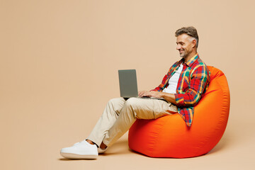 Full body adult IT man wear red shirt white t-shirt casual clothes sit in bag chair hold use work...