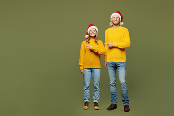 Full body smiling merry young couple two friends man woman wear sweater Santa hat posing point...