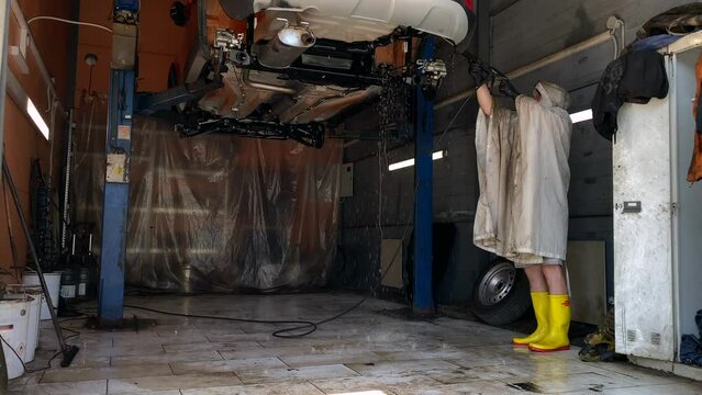 Professional washing of the rear arches of a car raised on a lift. A worker washes the wheel arches and beams behind the shock absorbers of a car. High quality 4K footage