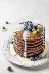 Chocolate pancakes with milk sauce and blueberries on white textured background. Delicious dessert for breakfast