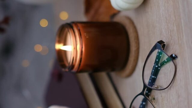 Autumn home disign: burning candle, with lights and glasses on table in cozy living room.Defocused.