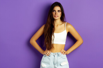 girl on a purple background. a young girl with long hair in a top and jeans is standing, a model girl is doing a photo shoot on a purple wall background