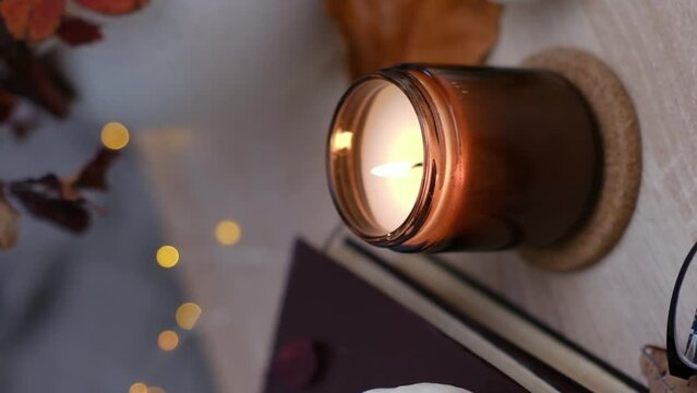 Autumn home disign: burning candle, with lights and glasses on table in cozy living room.