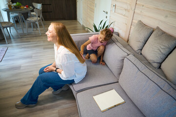 Mother sincerely laughing while little daughter combing her long blond hair