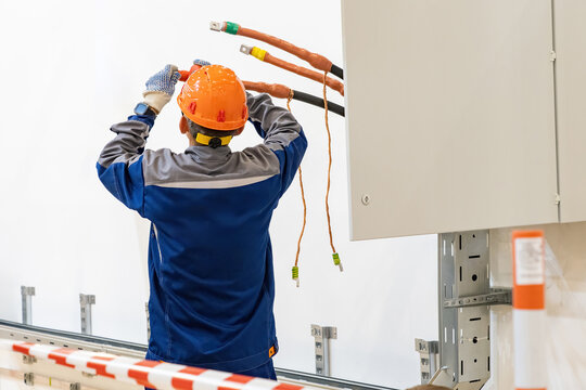 Electrician insulates power cables. Man editor with his back to camera. Electrician near power cabinet. Installation of grounding system for electrical equipment. Man electrician in hardhat