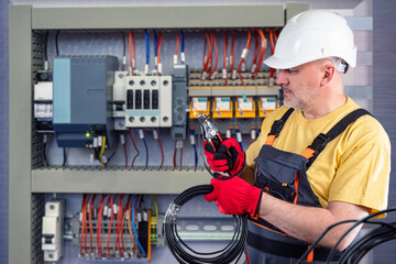 Electrical engineer. Man is repairing word cabinet. Guy with wire next to electrical panel. Electrician cuts cable with pliers. Electrical engineer in hardhat. Man repairman repairing power panel