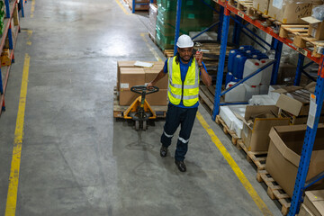African American man worker using pallet truck for move cardboard boxes. Storehouse employee in uniform working and unloading goods in warehouse. Logistics, Distribution Center concept.