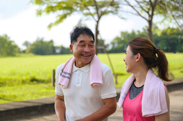 Asian Elderly Father and Daughter are walking relaxing in a green park, Breathing in the fresh air and enjoying the beautiful scenery. Healthcare and family bonding.