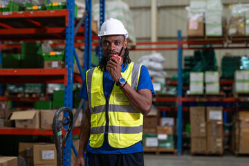 Black man warehouse worker wearing vest and helmet safety using portable radio talking with...