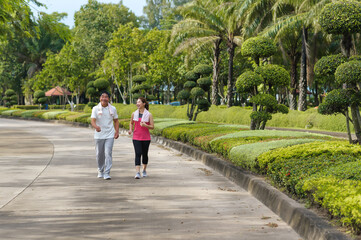 Fototapeta na wymiar Asian Elderly Father and Daughter are walking relaxing in a green park, Breathing in the fresh air and enjoying the beautiful scenery. Healthcare and family bonding.