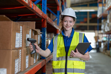Woman worker wearing vest and helmet safety with tablet using bar code scanner to scanning box on shelf checking stock inventory at warehouse factory store. Logistics, Distribution Center concept